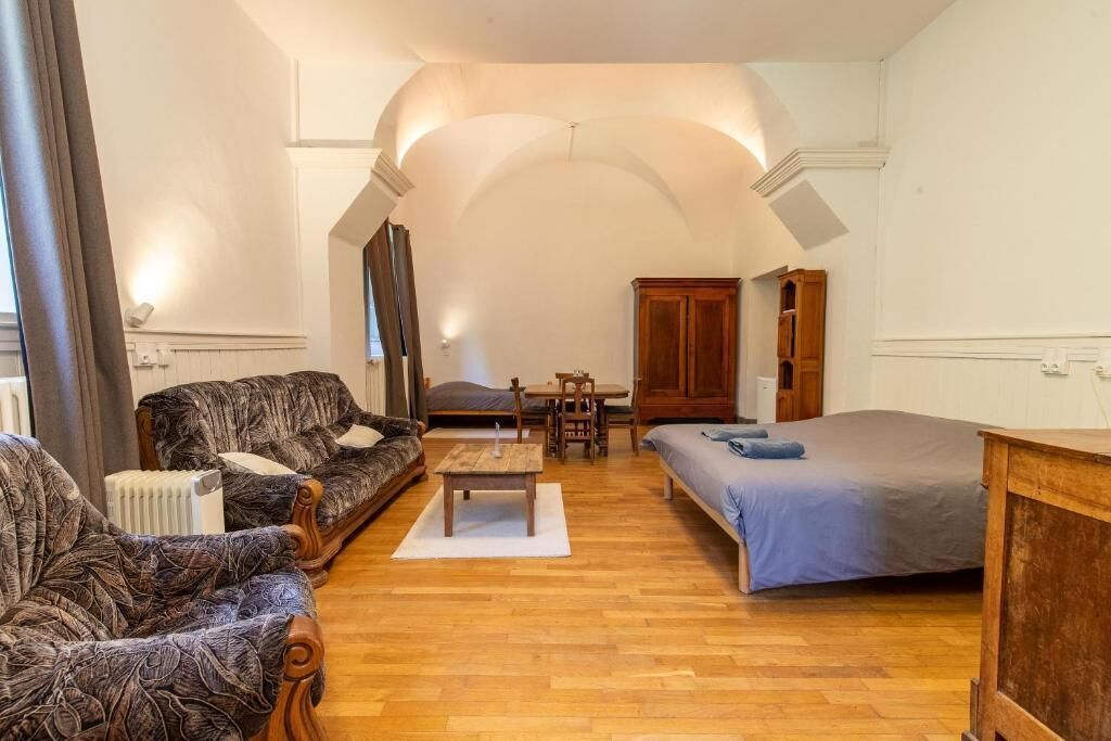 Ein Zimmer mit einer Couch, einem Bett, einem Holztisch, einem Schrank und einer Heizung.