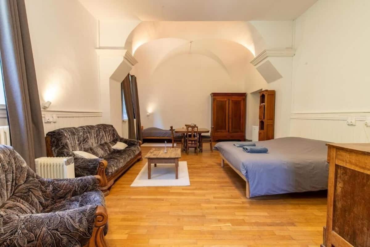 Une pièce comprenant un canapé, un lit, une table en bois, une armoire et un radiateur.