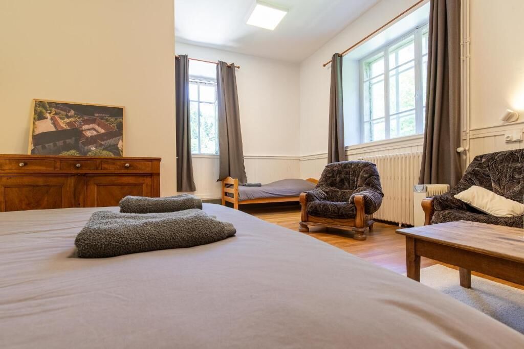Un dormitorio con una cama grande, un aparador de madera, una silla, una mesita y una ventana con cortinas.