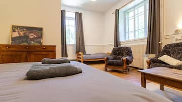 A bedroom with a large bed, a wooden dresser, a chair, a small table, and a window with curtains.
