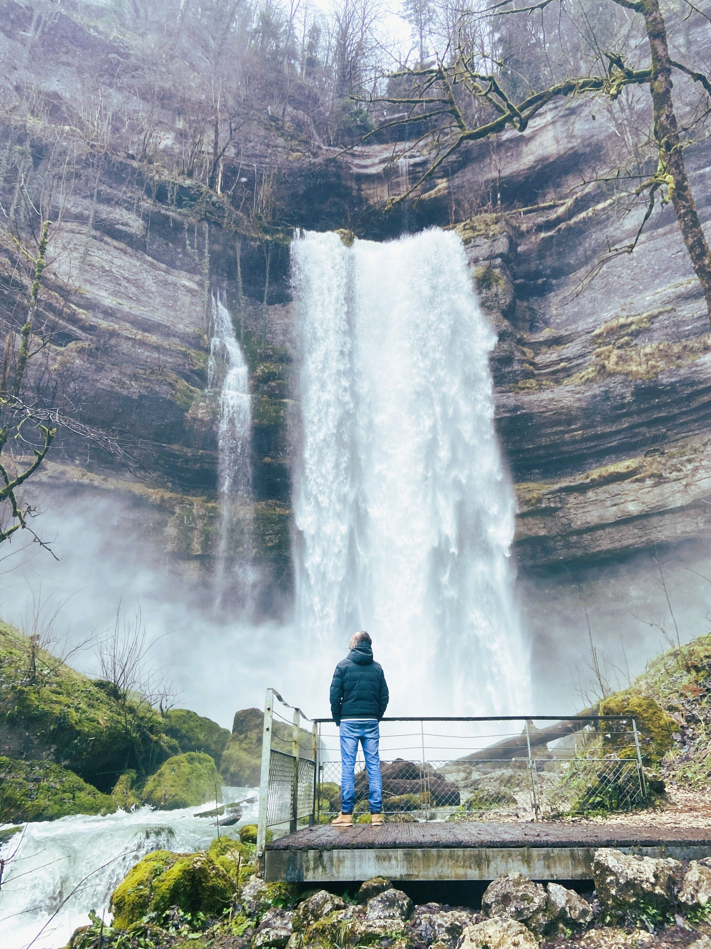A person standing on a platform observing a waterfall.