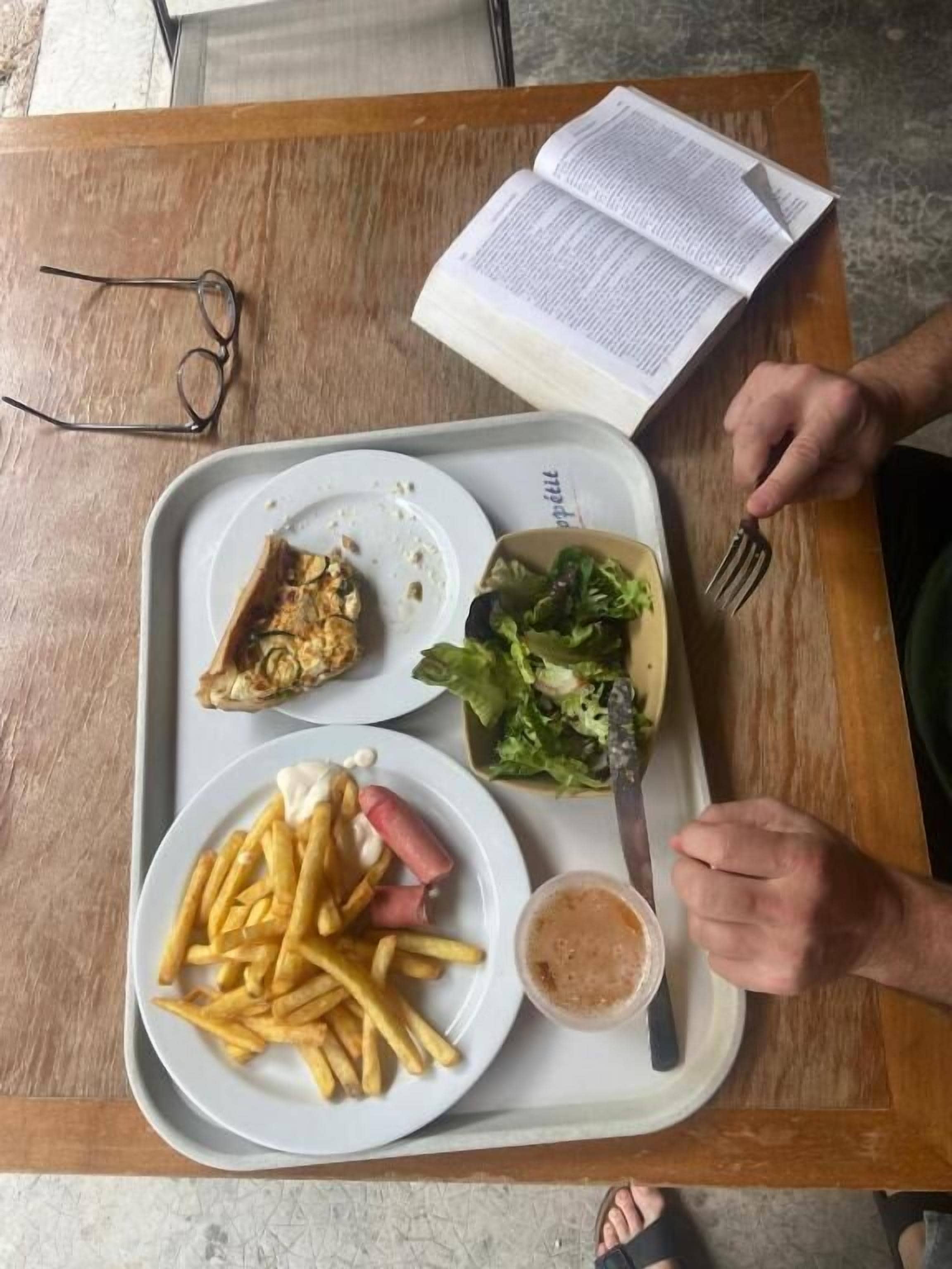 Ein Tablett mit Lebensmitteln, einem Buch und einer Brille auf einem Holztisch.
