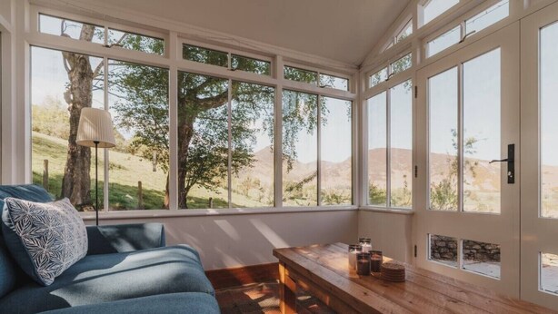 A room with a blue sofa, a wooden bench, and large windows offering a view of trees and hills.