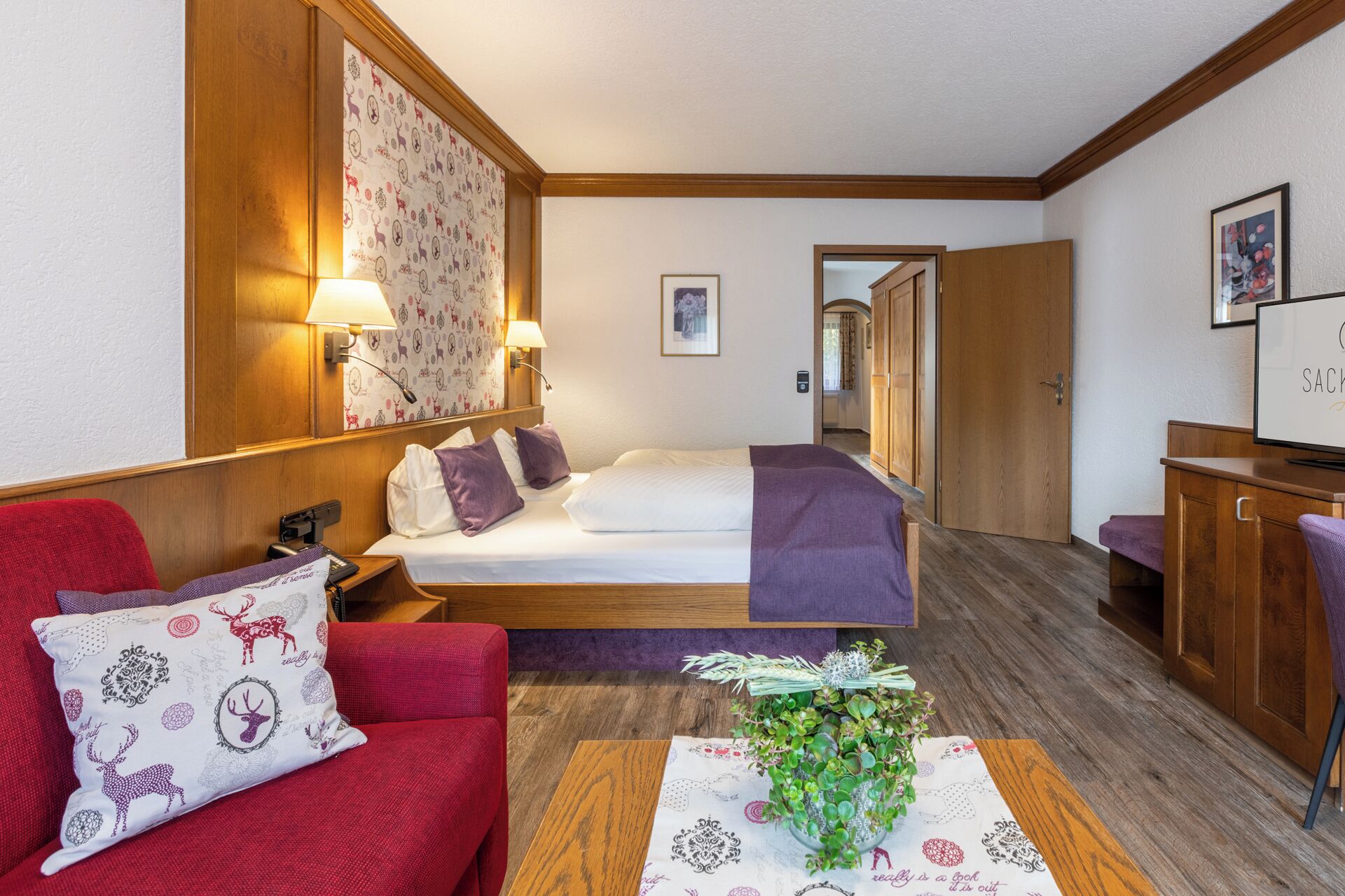 A hotel room with a bed, a red sofa, a wooden desk, and a mirror.