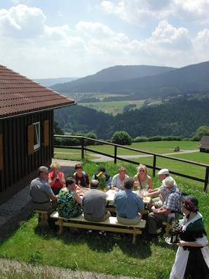 A group of people dining outdoors with a scenic view of hills and a wooden building in the background. - Sackmann Landhaus (Baiersbronn)