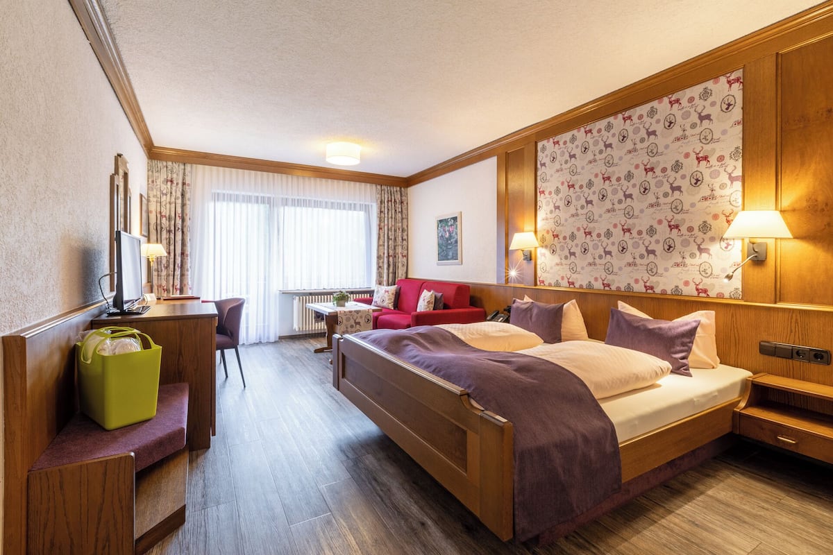Hotellihuone, jossa on sänky, työpöytä, tuoli, lamppu ja ikkuna, jossa on verhot.