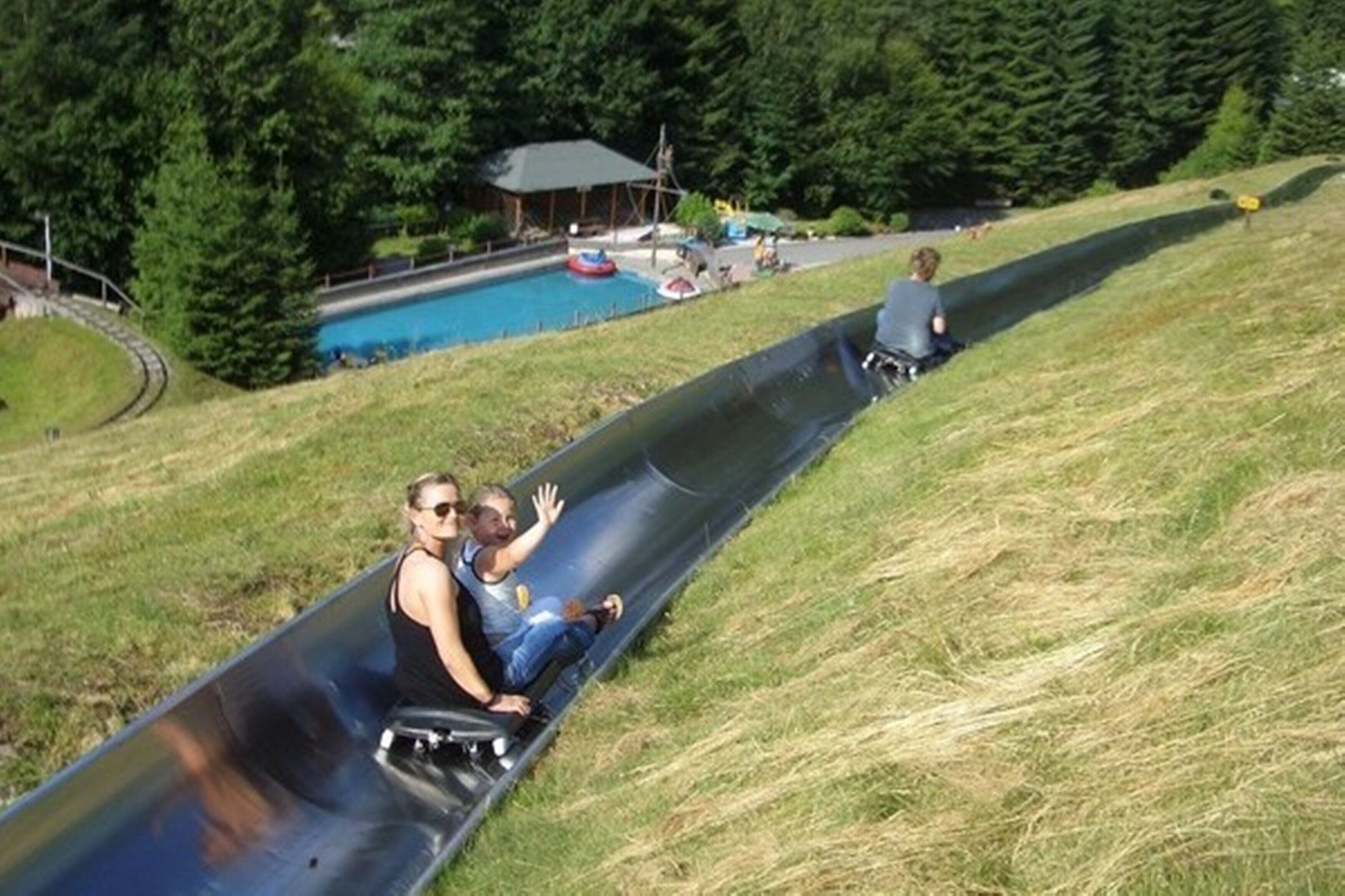 Una persona se desliza por un tobogán de metal, con una piscina al fondo.