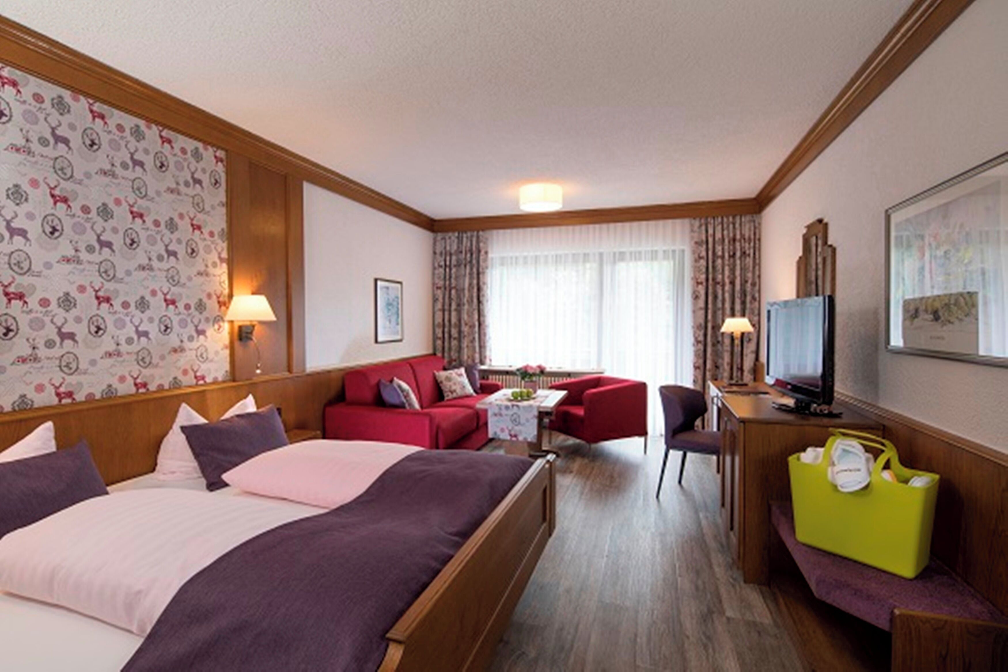 Ein Hotelzimmer mit einem Bett, einem roten Sofa, einem Schreibtisch mit Fernseher und einer grünen Tasche.