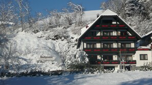 A traditional chalet-style building with a snow-covered roof, surrounded by a snowy landscape and trees. - Sackmann Landhaus (Baiersbronn)