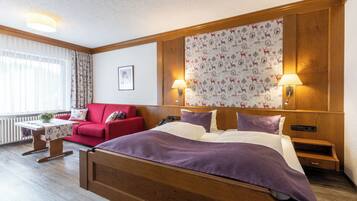Ein Hotelzimmer mit einem hölzernen Bett, einem roten Sofa, einem kleinen Tisch mit einer Lampe und einer Wand mit Muster.