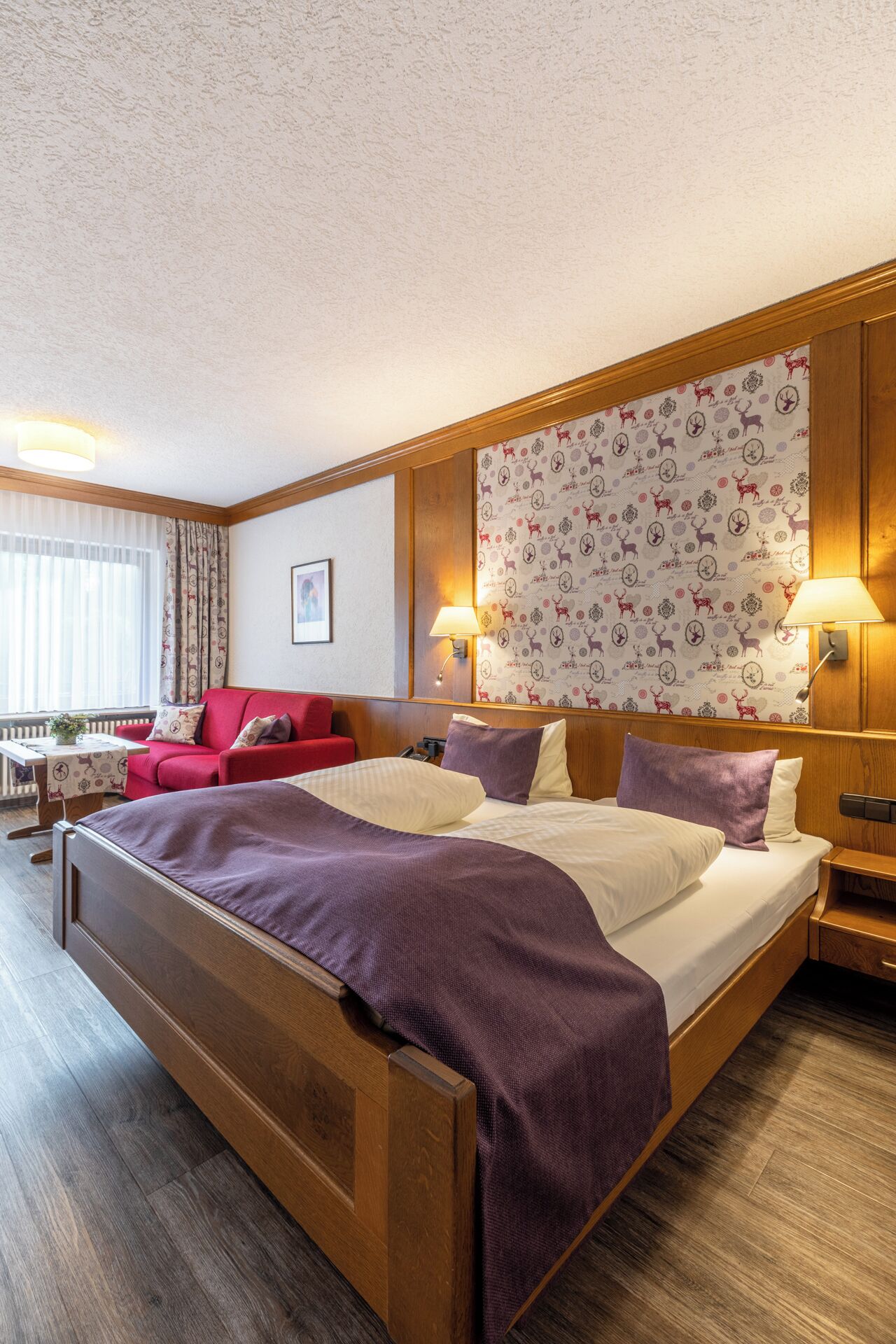 Ein Hotelzimmer mit einem großen Bett, einem roten Sofa, einem hölzernen Kopfteil und einer Wand mit Musterung.