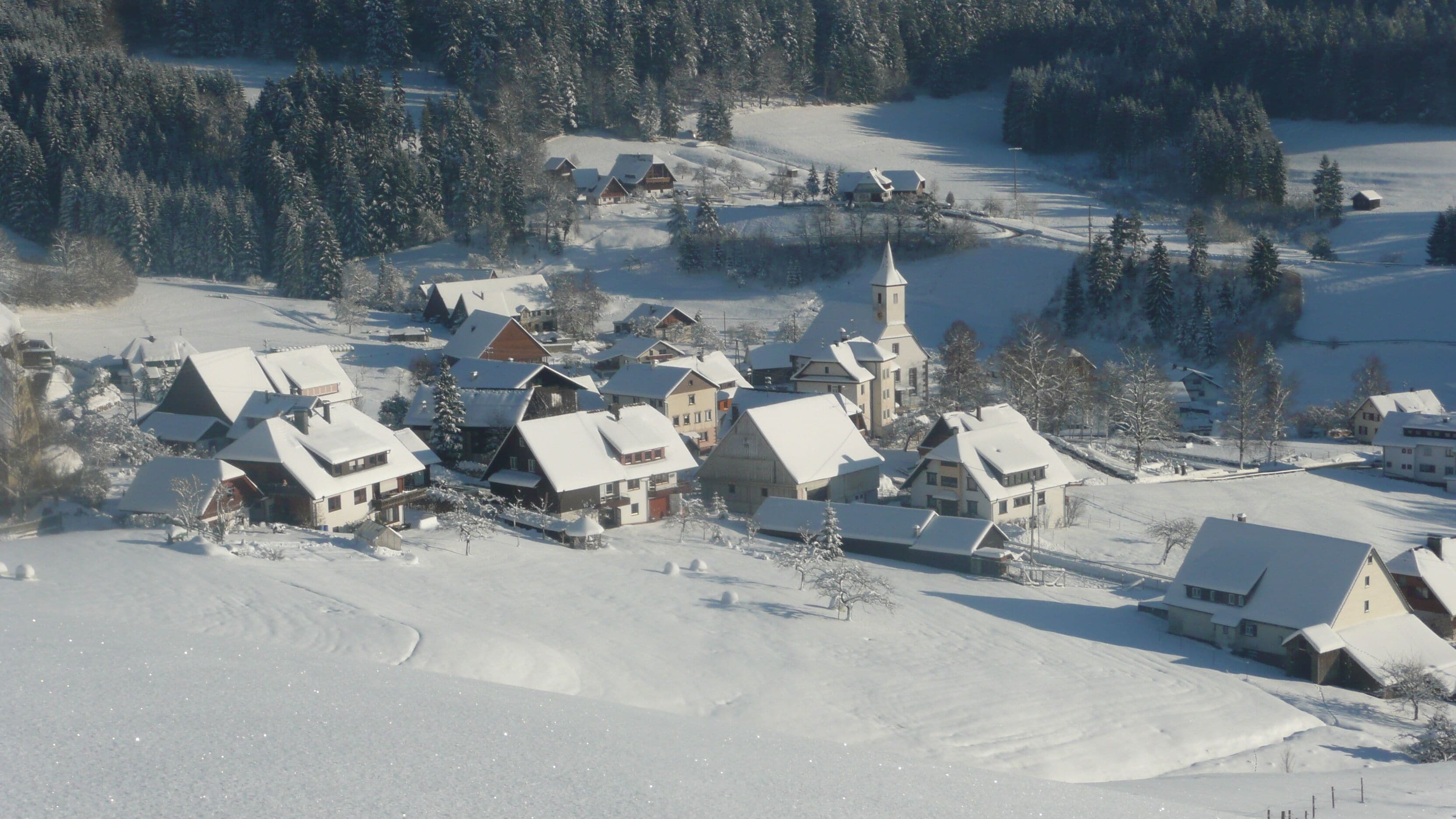 A snow-covered village with traditional houses, a church, and a clear sky.