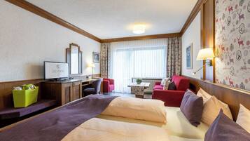 Habitación de hotel con cama, dos sillas, escritorio, televisor y ventana con cortinas.