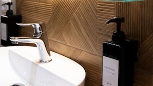 Un baño con un lavamanos blanco, un grifo cromado, un dispensador de jabón y un estante de vidrio.