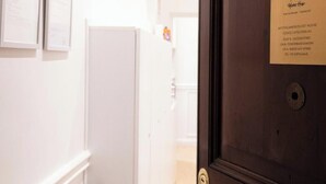 Una habitación de hotel con una puerta de madera, una pared blanca con un certificado enmarcado y un paraguas negro apoyado contra la pared.