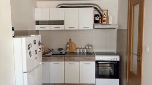 A compact kitchen with white cabinets, a built-in oven, and a refrigerator. - Sky and Sea View Apartment in Budva (Budva)