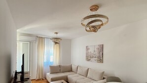 A modern living room with a sofa, a coffee table, a TV, and a dining area with chairs. - Sky and Sea View Apartment in Budva (Budva)