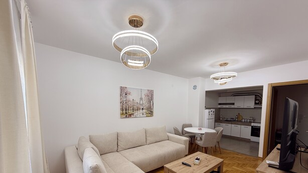 A modern living room with a sectional sofa, a coffee table, and a dining area with a white table and chairs. - Sky and Sea View Apartment in Budva (Budva)