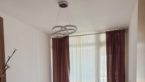 A bedroom with a bed, a ceiling light fixture, a window with curtains, and a wooden floor. - Sky and Sea View Apartment in Budva (Budva)