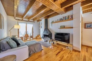 Un salon chaleureux avec une cheminée, un téléviseur et des poutres en bois au plafond.