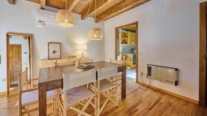 Uma sala de jantar com uma mesa e cadeiras de madeira, um lustre pendurado e um radiador fixado na parede.