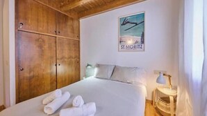 Quarto de hotel com cama, guarda-roupa de madeira, quadro na parede e mesa de cabeceira com abajur.