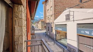 Uma rua estreita com edifícios de pedra, uma varanda e uma loja com um letreiro.