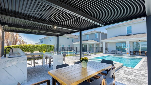 Un espacio exterior techado con piscina, una mesa de madera con sillas y una parrilla.