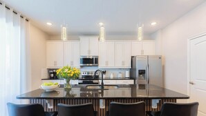Una cocina moderna con gabinetes blancos, una isla central con taburetes de bar, un refrigerador y un microondas.
