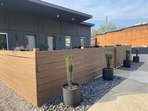 A modern building with a grey facade, wooden fence, and potted plants.