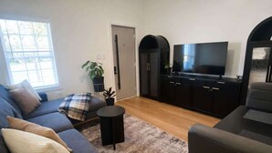 Uma sala de estar com sofá, poltrona, televisão e uma mesinha.