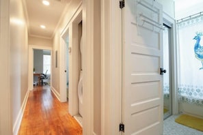 A hallway with wooden flooring, white walls, and a closed door with a peacock-themed curtain. - Civil Rights Trail Townhome - Near Historic Sites (Montgomery)