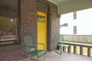 A porch with two green chairs, a yellow door, and a brick wall. - Civil Rights Trail Townhome - Near Historic Sites (Montgomery)