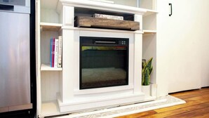Una llar de foc blanca amb una porta de vidre, envoltada d'estantes blanques i una petita planta.