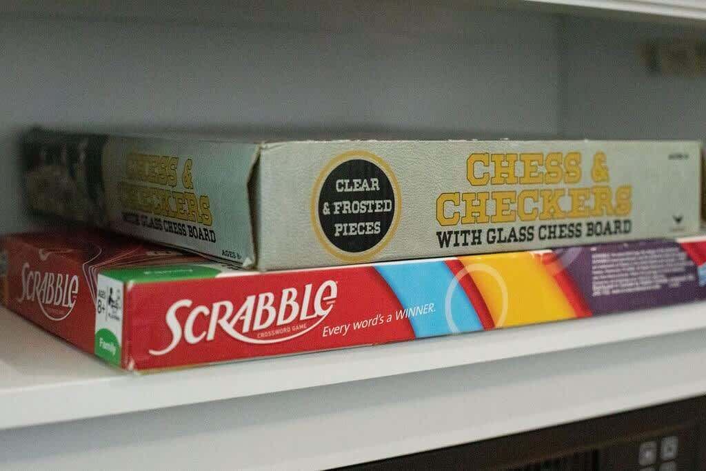 A shelf with board games including Scrabble, Checkers, and Chess & Checkers with a glass board.