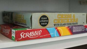 A shelf with board games including Scrabble, Checkers, and Chess & Checkers with a glass board.