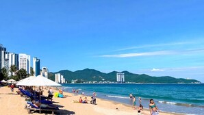 A beach with umbrellas, lounge chairs, and people.
