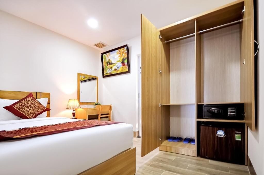 Una habitación de hotel con una cama, un armario de madera, un escritorio con lámpara y un cuadro en la pared.