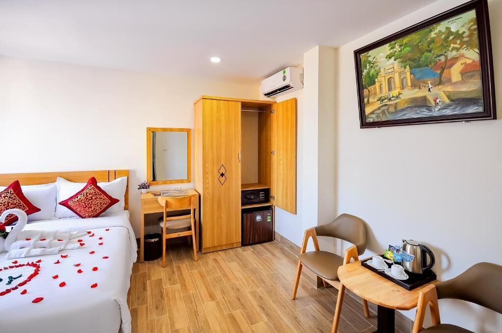 A hotel room with a bed, desk, chair, and a painting on the wall.