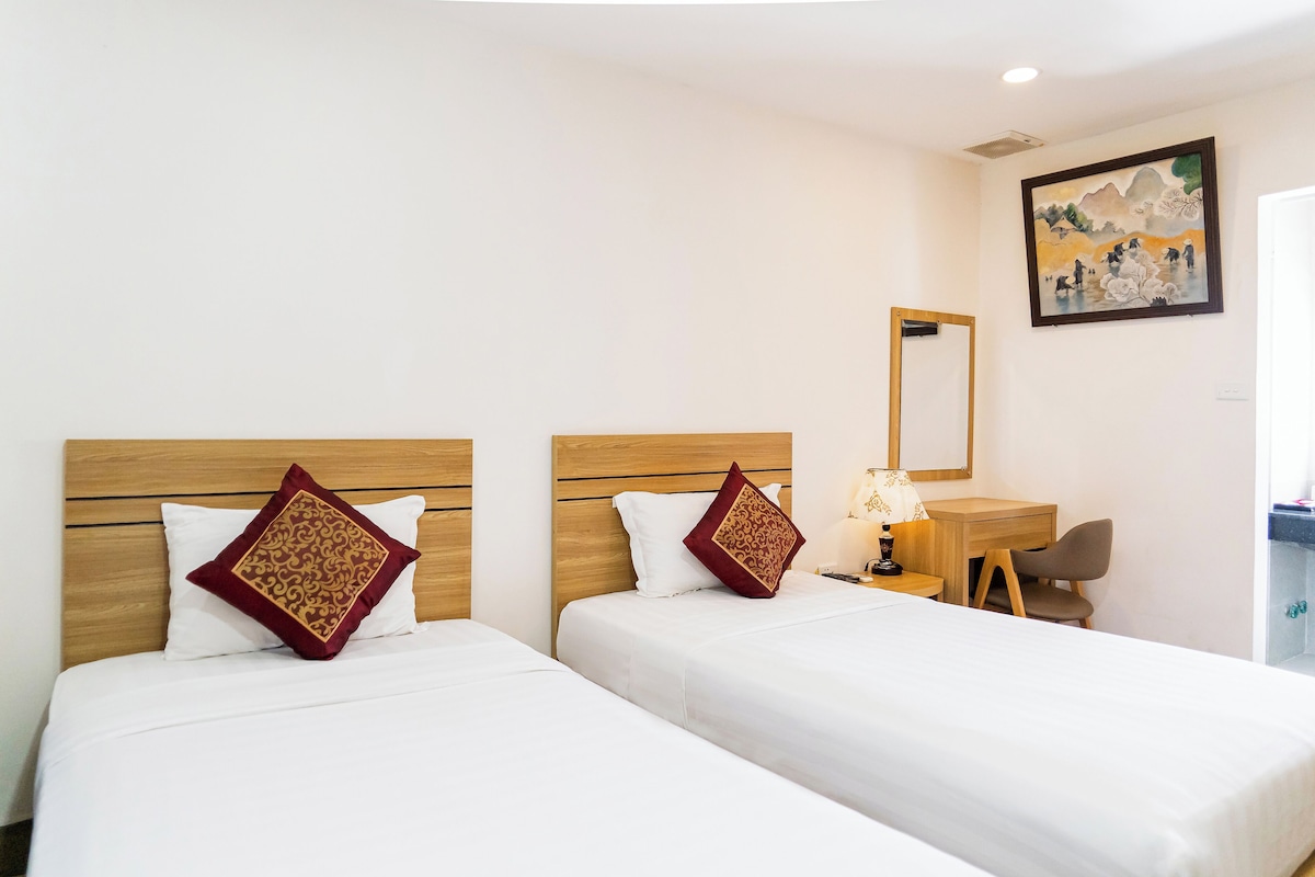 Quarto de hotel com duas camas, uma escrivaninha, uma cadeira e um quadro na parede.