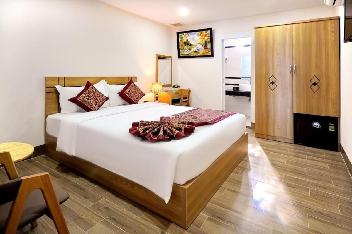 Quarto de hotel com cama, escrivaninha, cadeira, guarda-roupa e um quadro na parede.