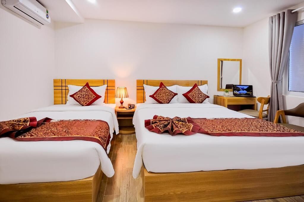 A hotel room with two beds, a desk, a chair, a TV, and a window with curtains.