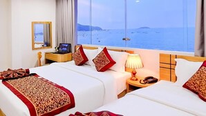 A hotel room with two beds, a desk, a lamp, a phone, and a view of the sea.