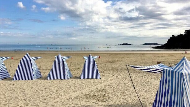 Ein Strand mit gestreiften Sonnenschirmen und sandigem Ufer.