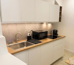 Eine moderne Küche mit einer Spüle aus Edelstahl, einer schwarzen Mikrowelle und einer Kaffeemaschine auf einer Holzauskleidung.