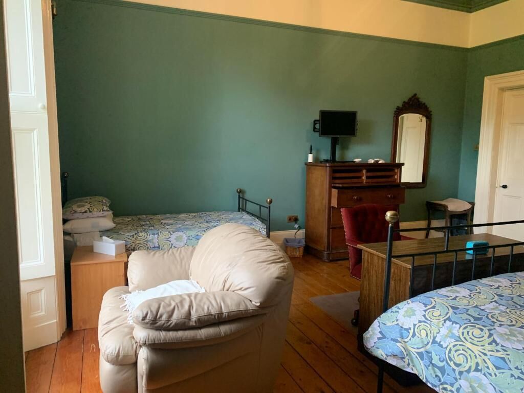 A bedroom with a bed, a chair, a dresser, a television, and a mirror.