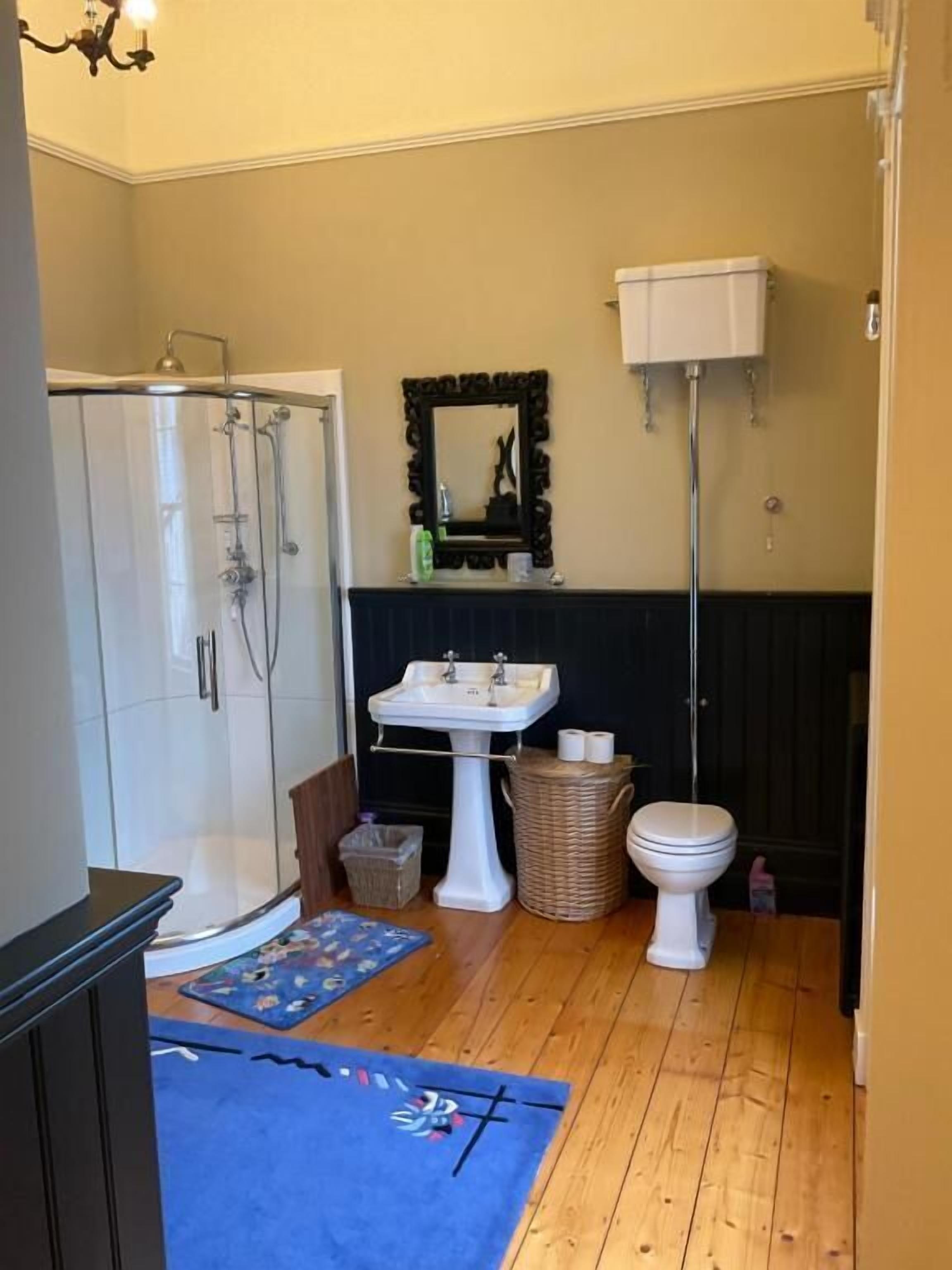 A bathroom with a shower, sink, toilet, and a mirror.