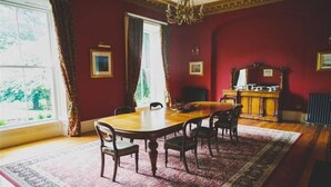 A room with a wooden dining table, chairs, a chandelier, a radiator, and a window with curtains. - Ballynacree Manor House  (Ballymoney)