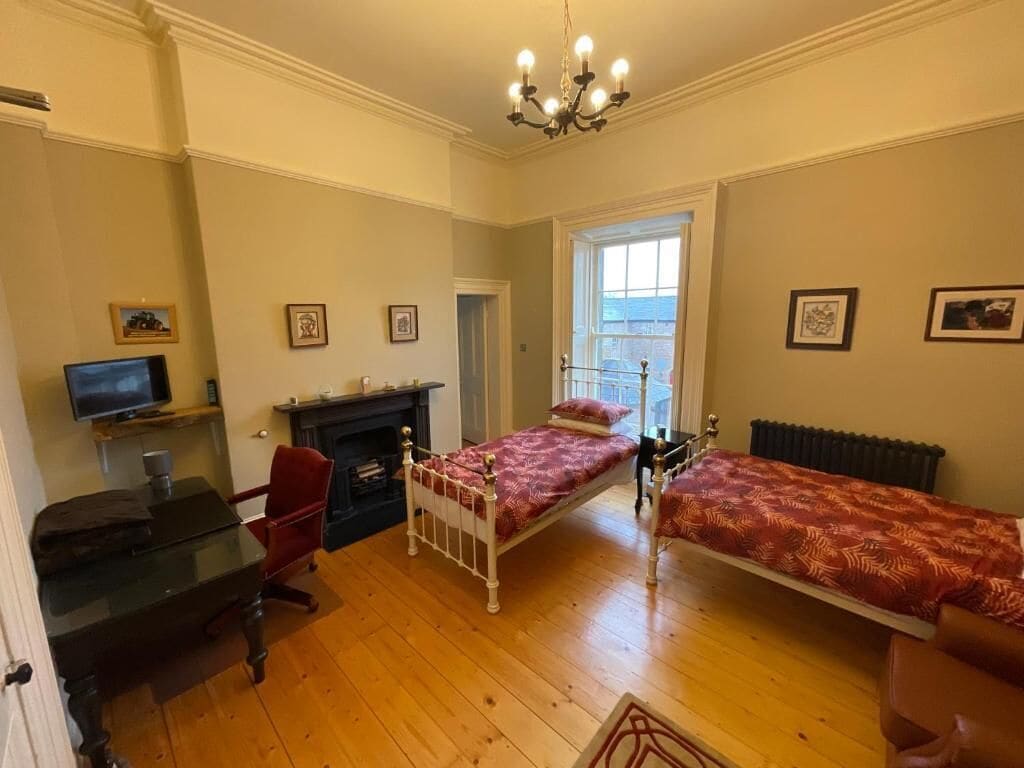 A room with two beds, a desk, a chair, a television, and a fireplace.