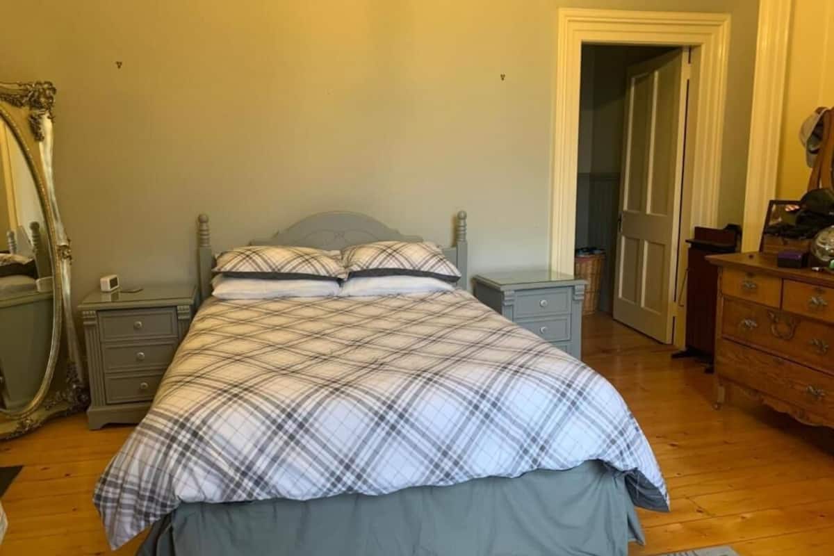 A bedroom with a bed, nightstands, a dresser, a mirror, and a door leading to another room.